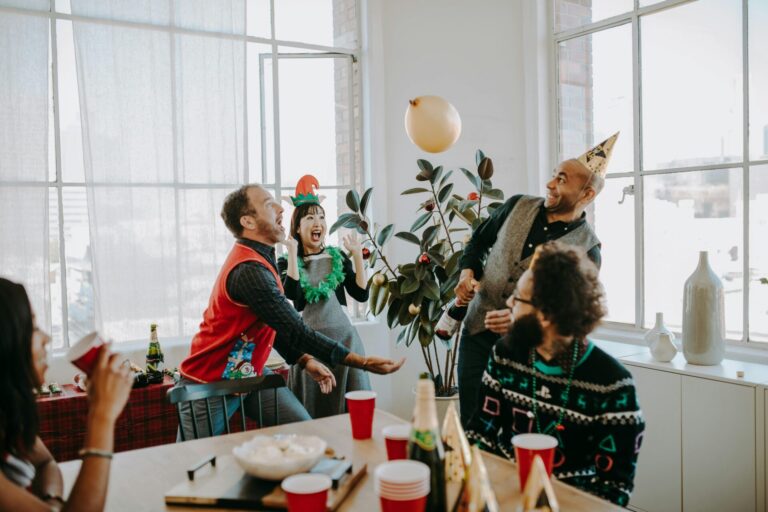Cheerful office holiday party with adults in festive Christmas sweaters celebrating with food and drinks.