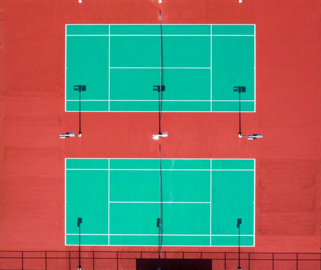 Bright aerial shot of two tennis courts on a sunny day.