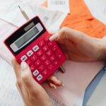 Close-up of hands holding a red calculator, managing finances with documents and receipts.