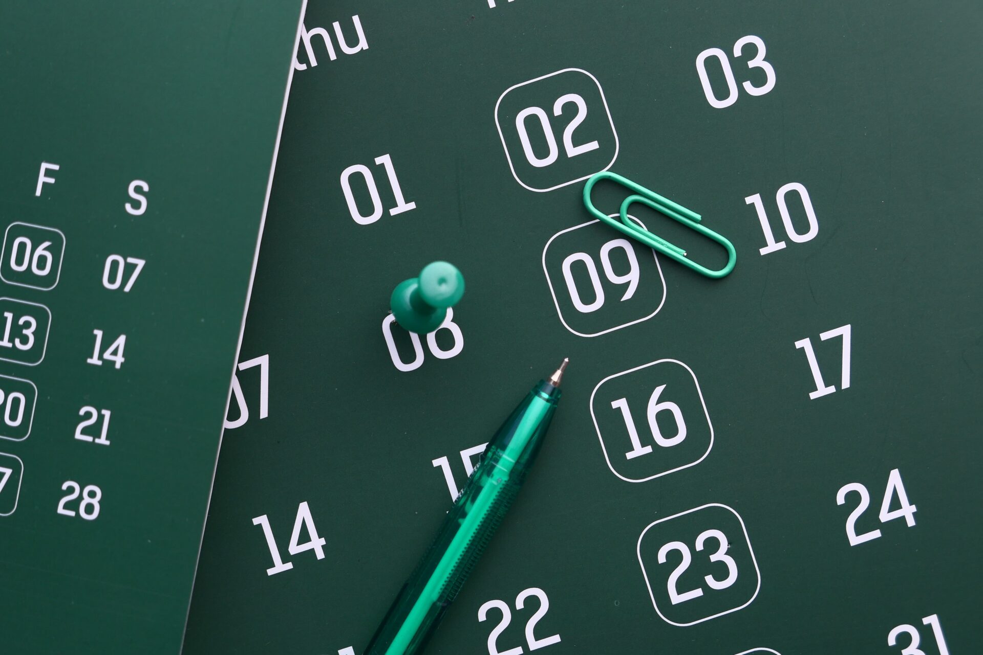 Planning Guides 3 Close-up of a green calendar with pen, push pin, and paper clip for planning and organization.