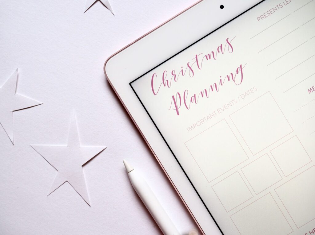 Top view of a tablet with Christmas planning template and stars on a white surface.