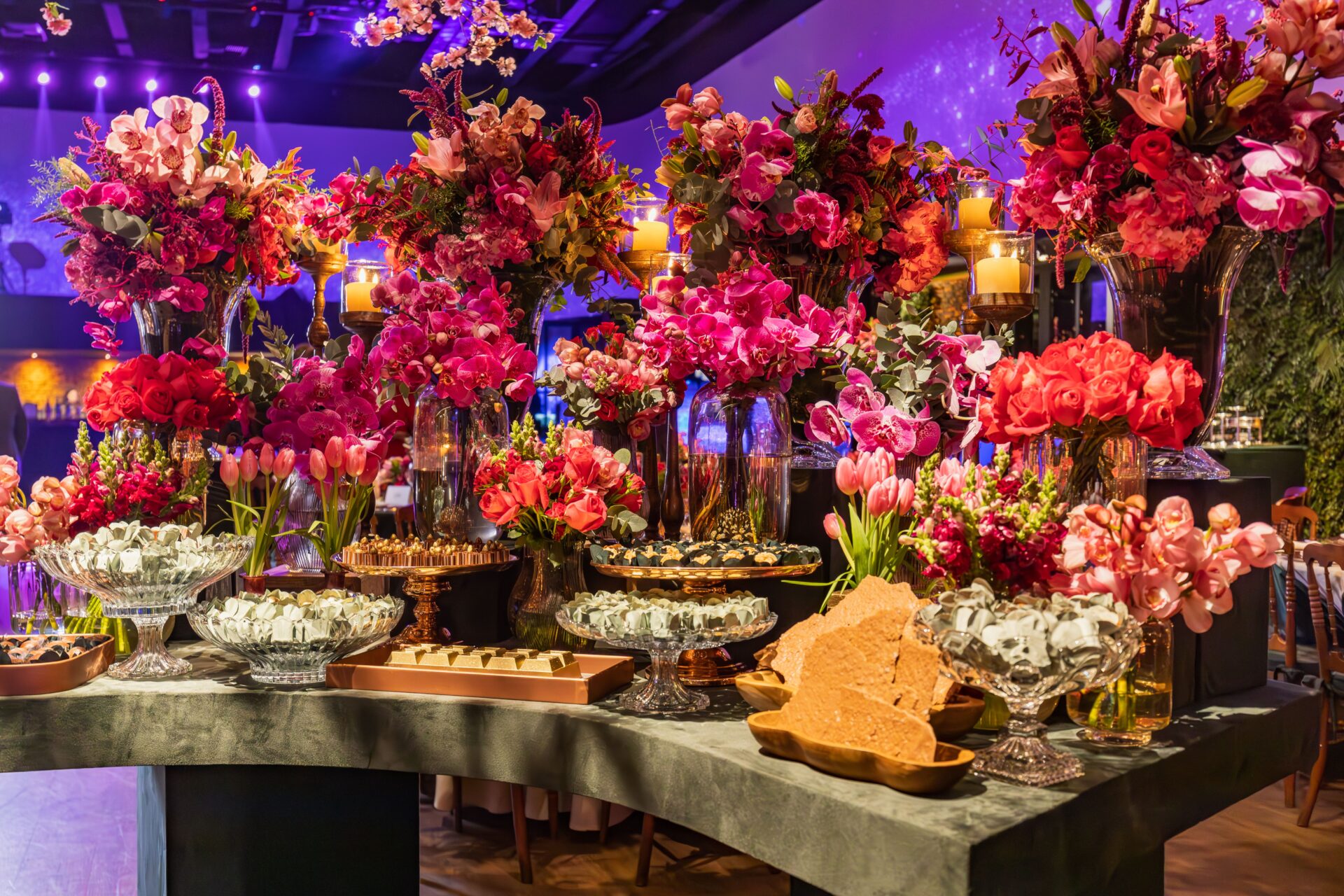 Lavish floral arrangement and desserts on a decorated table with candles in an indoor setting.