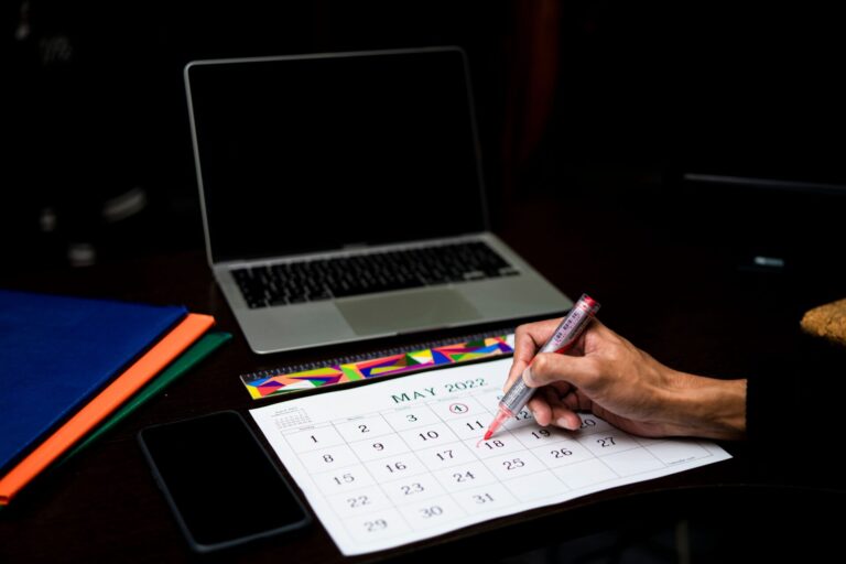 A person plans on a calendar at a desk with a laptop and phone, May 2022.