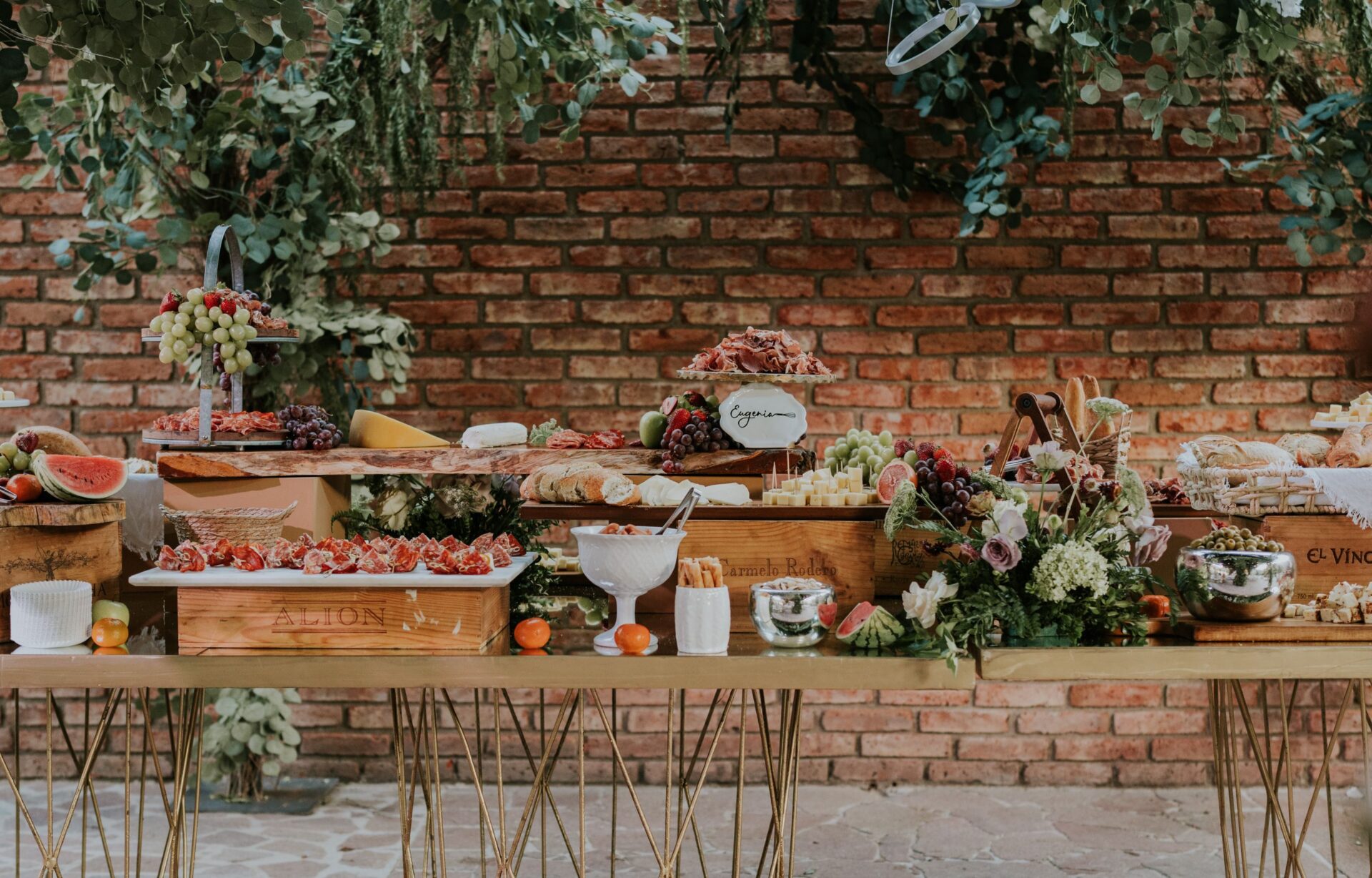 Elegant outdoor buffet setting with an array of foods and floral decorations against a brick wall.