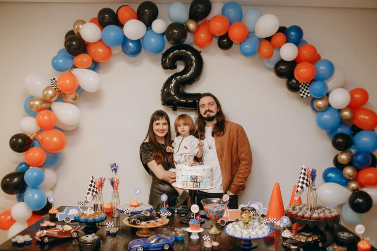 Family celebrating a child's birthday with balloons and cake indoors.