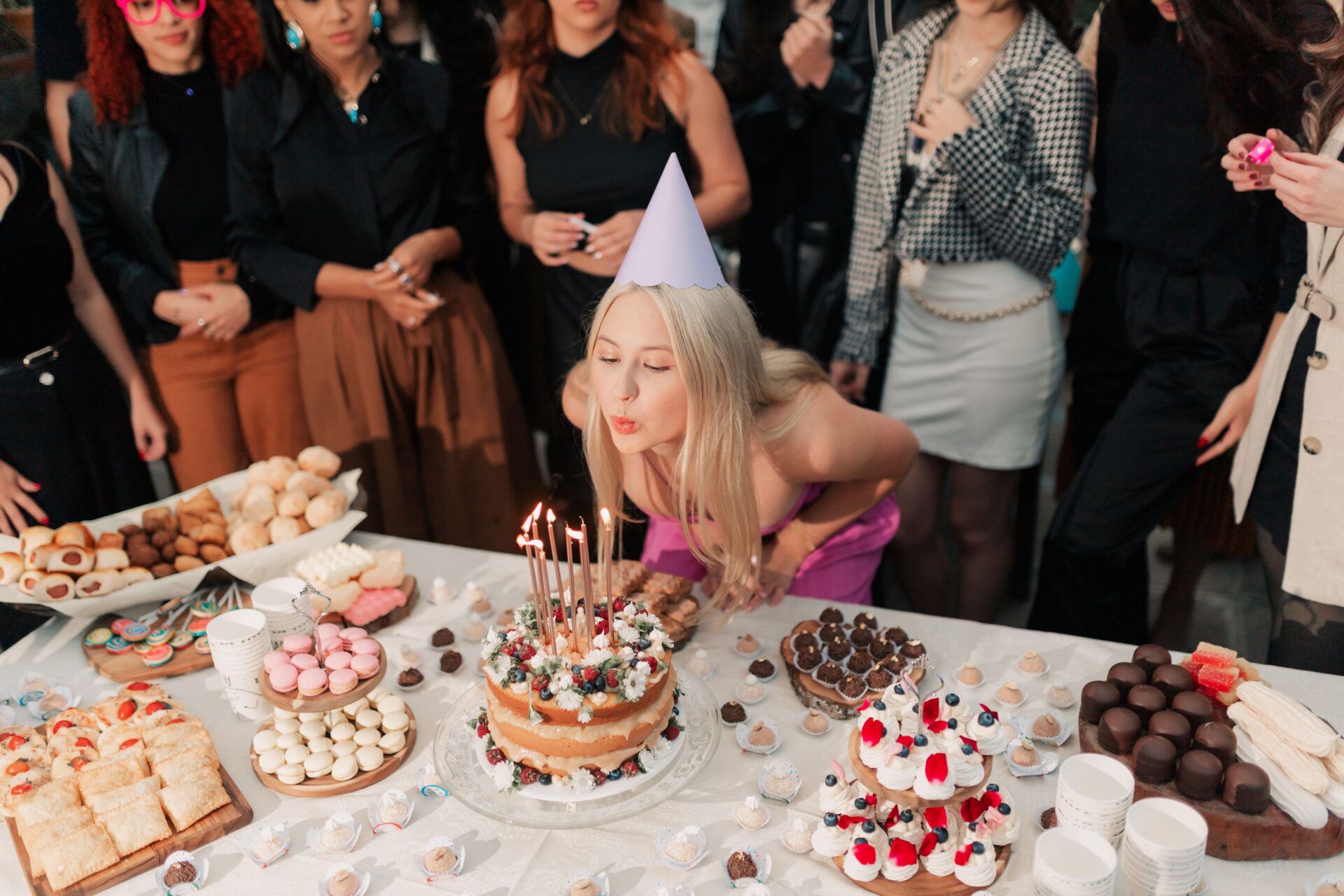 Home 17 A cheerful young woman celebrates her birthday, surrounded by friends and a variety of delicious cakes and desserts.