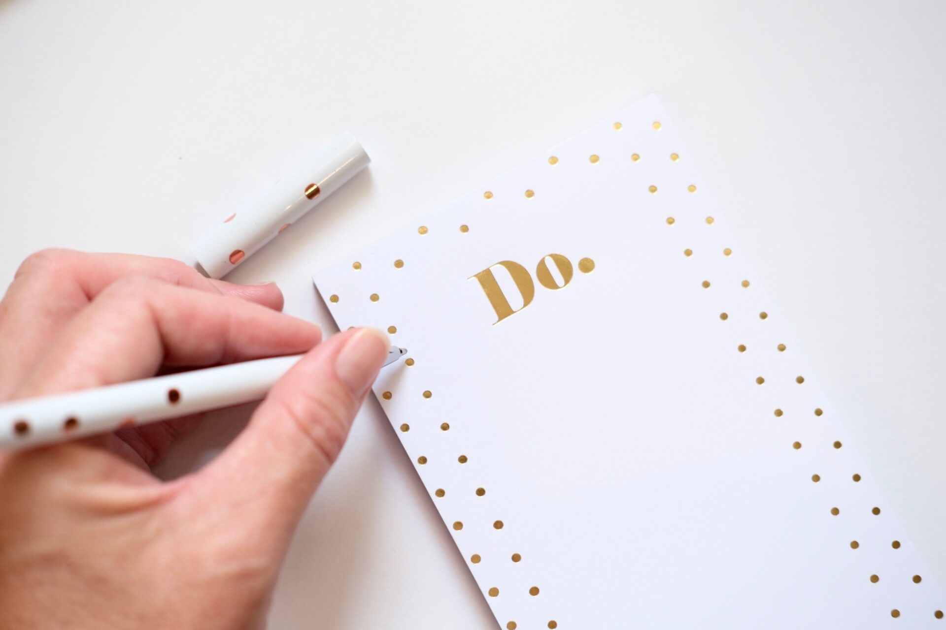 Close-up of a hand writing on a chic to-do list with gold polka dots using a stylish pen.