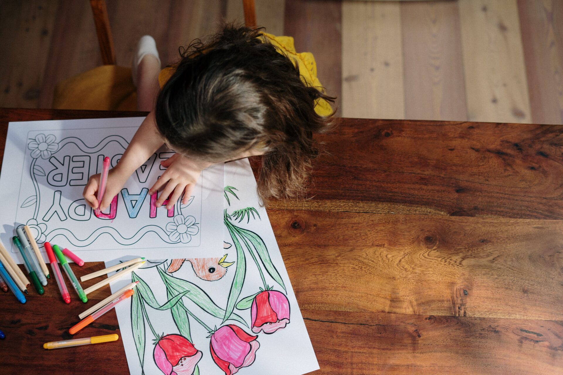 COLORING PAGES 2 A child creatively colors Easter-themed artwork with vibrant markers on a wooden table.