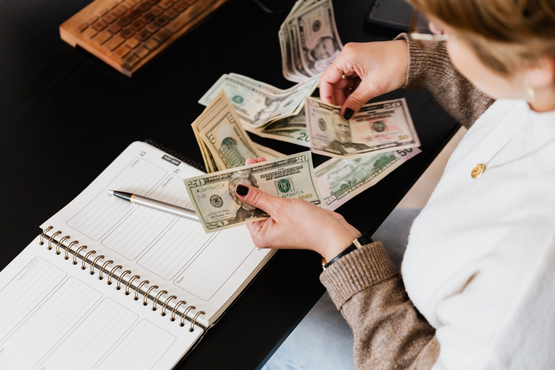 Planning Guides 2 Woman organizing finances, counting dollar bills at desk with open notebook.