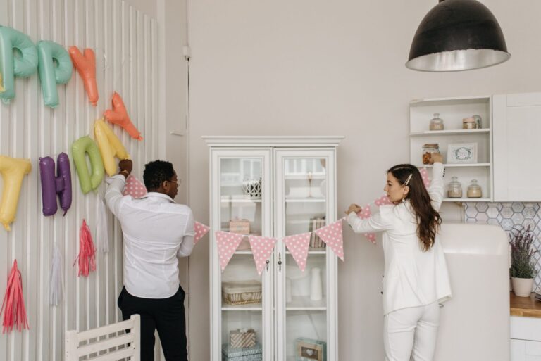 Two adults decorating a room with balloons and banners for a birthday party.