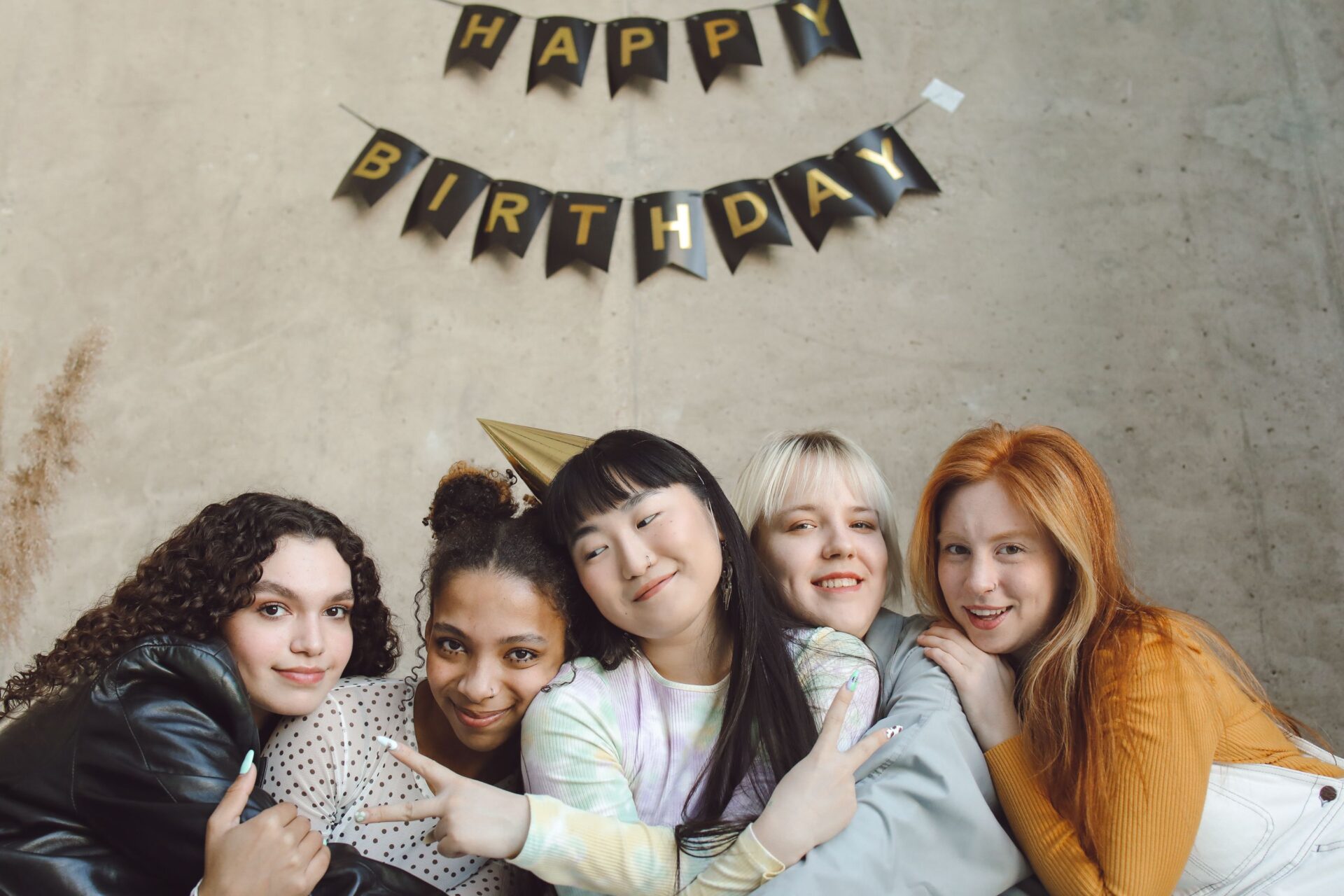 A group of smiling young women celebrating a birthday with a festive banner.