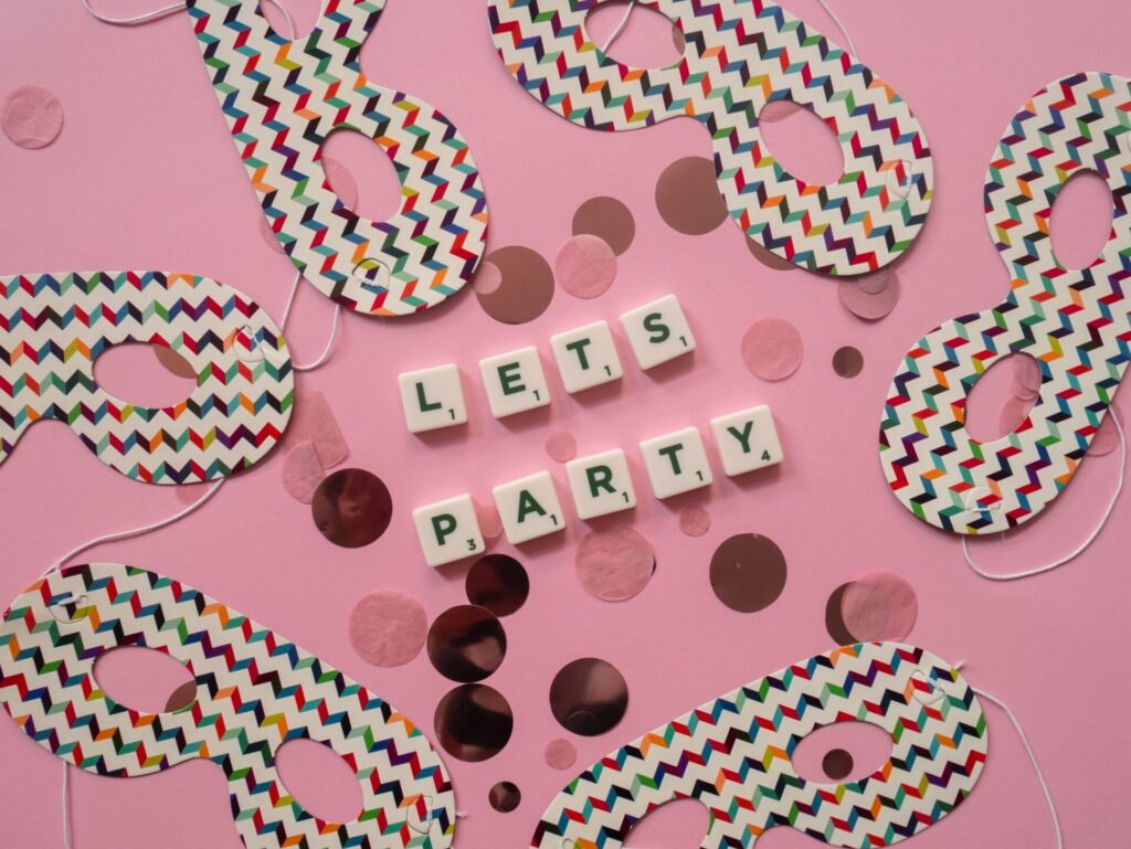 Flat lay of themed party masks and 'Let's Party' text on a pink surface.