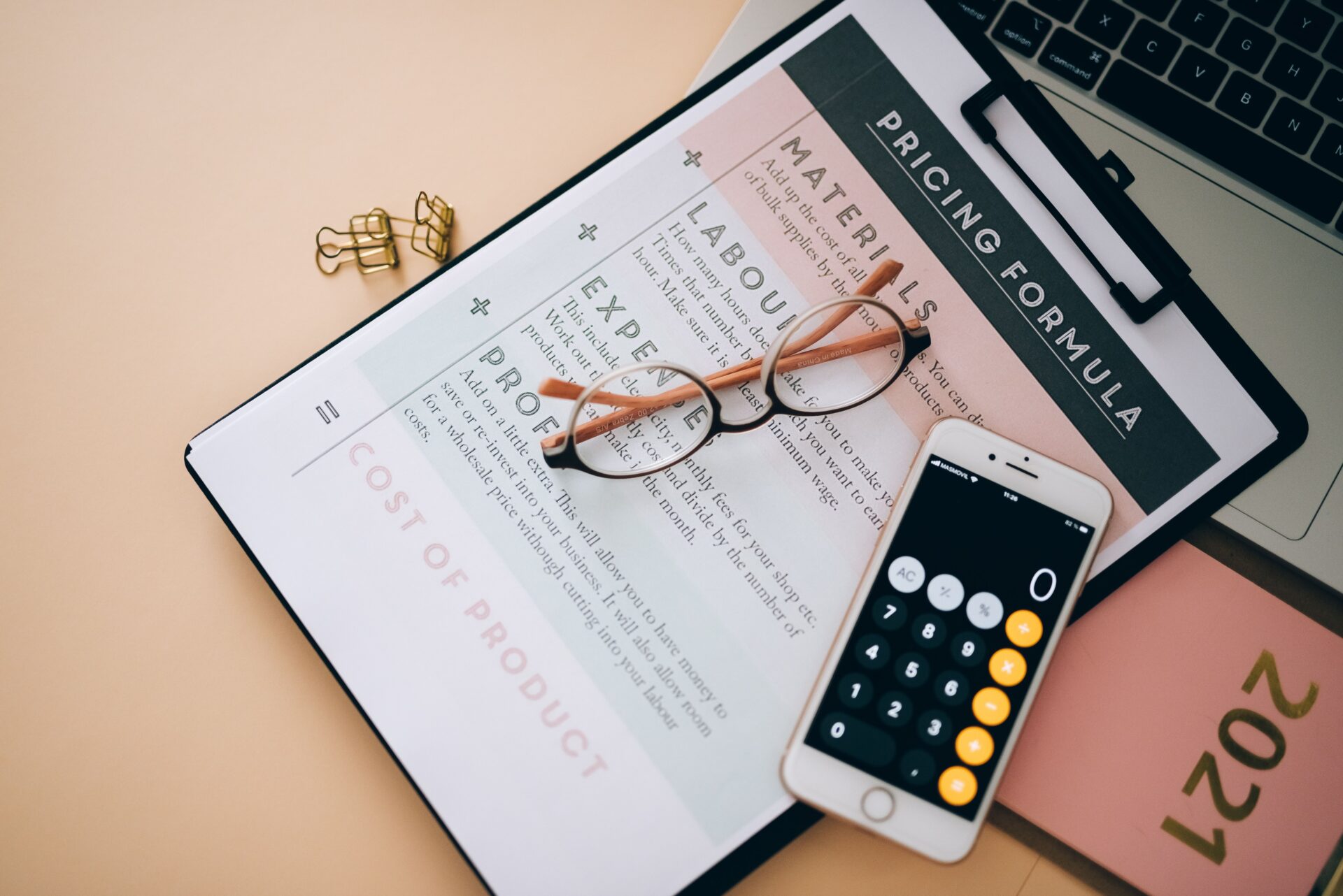 Marketing 4 Overhead view of business tools including a phone calculator, pricing formula document, and eyeglasses on a desk.