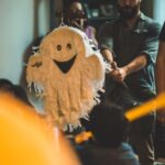 A festive Halloween party with guests enjoying a ghost-shaped pinata indoors.