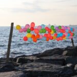 Vibrant balloons tied by the ocean, creating a serene sunset scene.