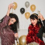 Cheerful friends with glasses of tasty champagne smiling and congratulating each other among balloons