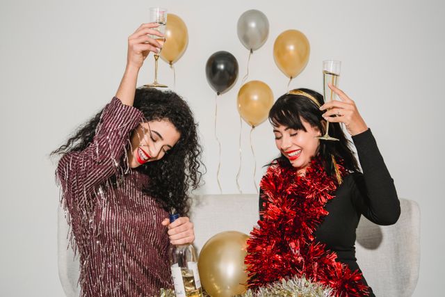 Cheerful friends with glasses of tasty champagne smiling and congratulating each other among balloons